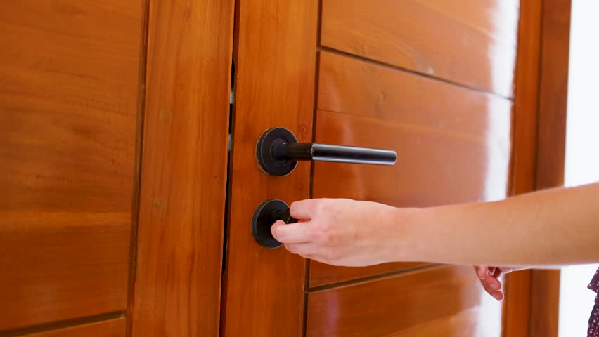 A woman unlocks a wooden door with a key and pushes it open indoors