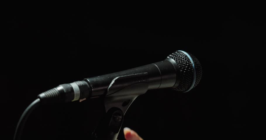 Close-up of hands adjusting a microphone on a black background. Concept of music, performance, audio setup and stage preparation.