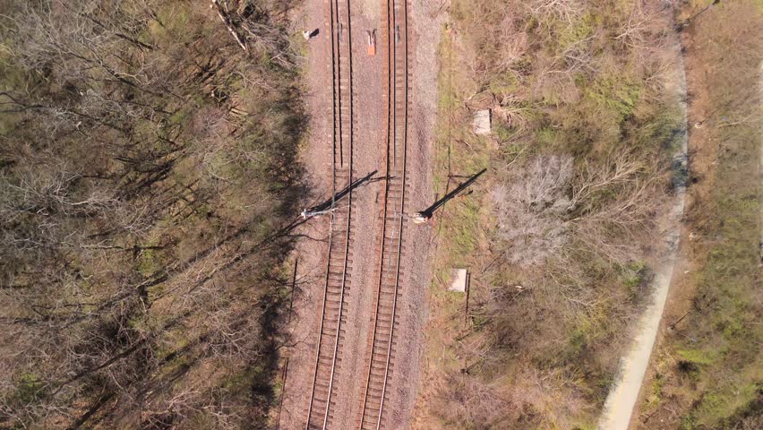 Aerial top down view of railway tracks through trees and curved road
