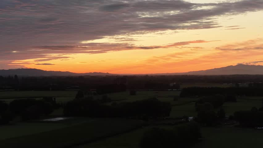 Aerial dusk view of glowing horizon over dark rural landscape and mountains near Hamilton