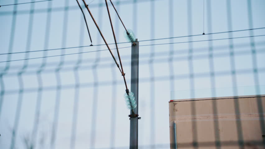 Passenger train passing through, framed by overhead electric cables and surrounding buildings