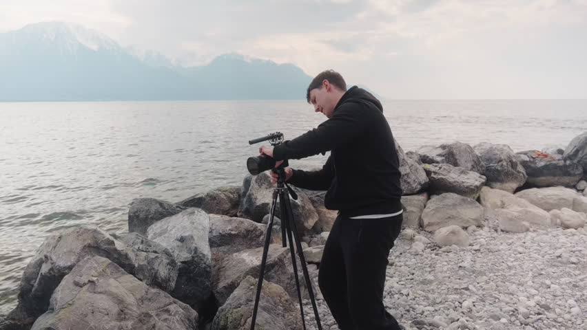 Photographer setting up a camera on a tripod next to a lake at a beach during the day, gimbal shot