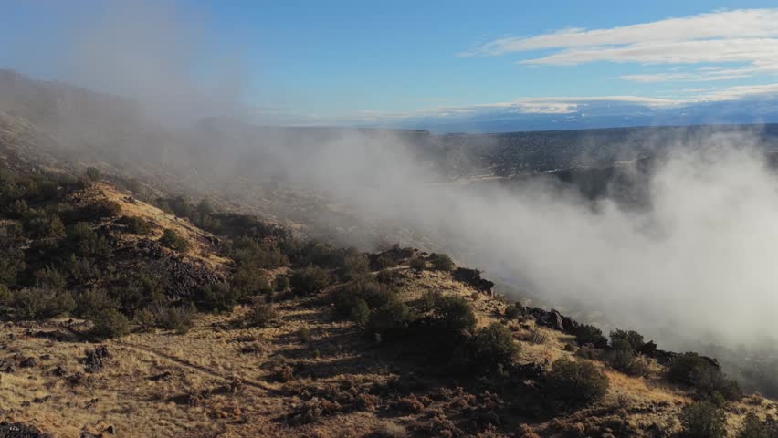 Drone shot of thick mist captured forming and swirling within a deep canyon gorge. This aerial view shows the natural development of clouds over a rugged and rocky remote wilderness environment.