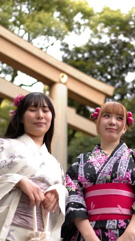 Low angle shot of two friends in kimonos smiling before a wooden torii gate
