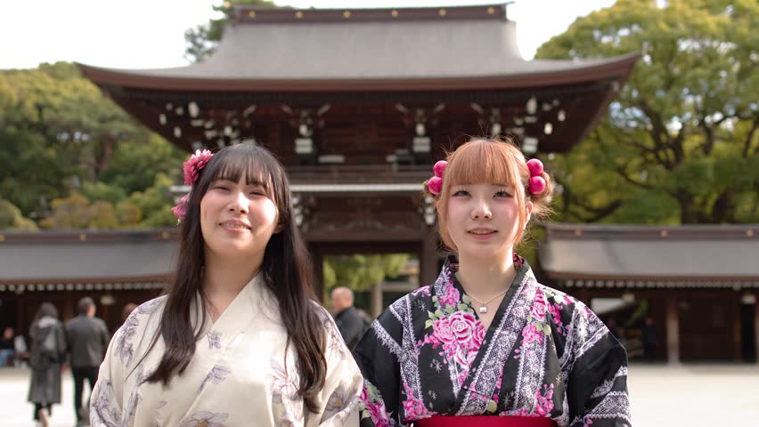 Two women wearing traditional kimono stand before a historic shrine gate in Tokyo, Japan