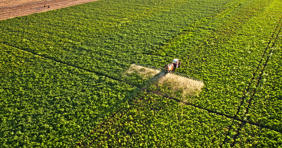 Aerial view of a tractor with a boom sprayer applying chemicals to a lush green agricultural crop