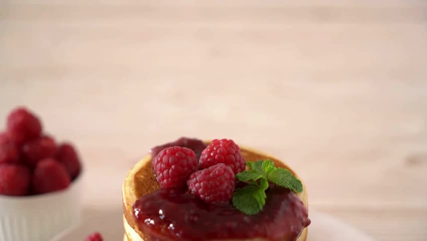 putting honey or jam on pancakes with raspberries. tasty pancakes with berries. A stack of fluffy breakfast American pancakes with fresh raspberries.