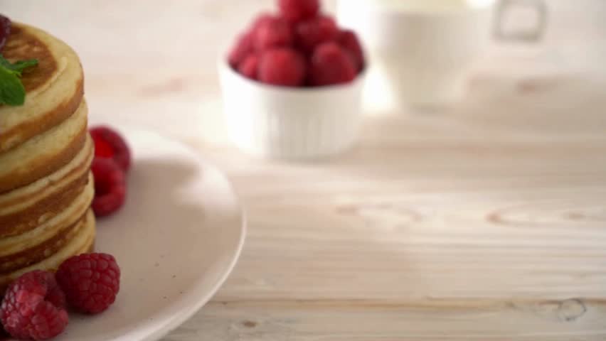 putting honey or jam on pancakes with raspberries. tasty pancakes with berries. A stack of fluffy breakfast American pancakes with fresh raspberries.