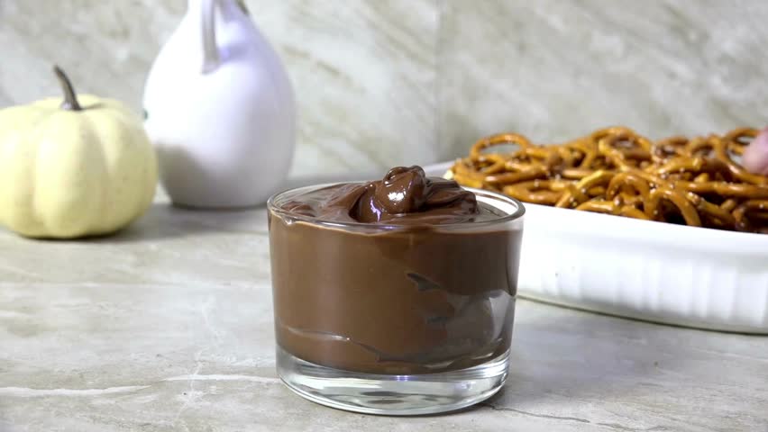 Hand Dipping a salted mini pretzel into melted milk chocolate sauce. Chocolate sauce and salted pretzels. Tasty mini pretzel with dark chocolate dipping sauce.