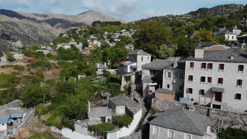 Stone houses dot a lush mountainside in Kalarrytes, Greece. The serene landscape offers a glimpse into traditional Greek architecture. Ideal for travel and cultural documentaries.