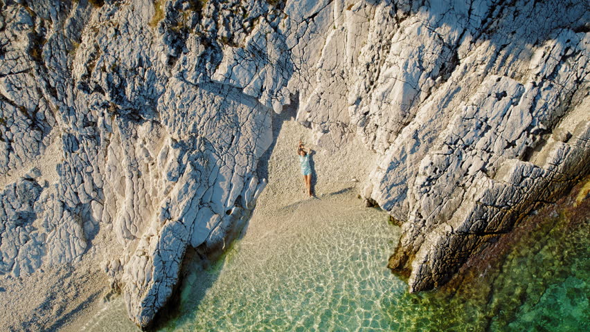 Aerial view of woman lying on pebble beach between rocky cliff and sea in summer