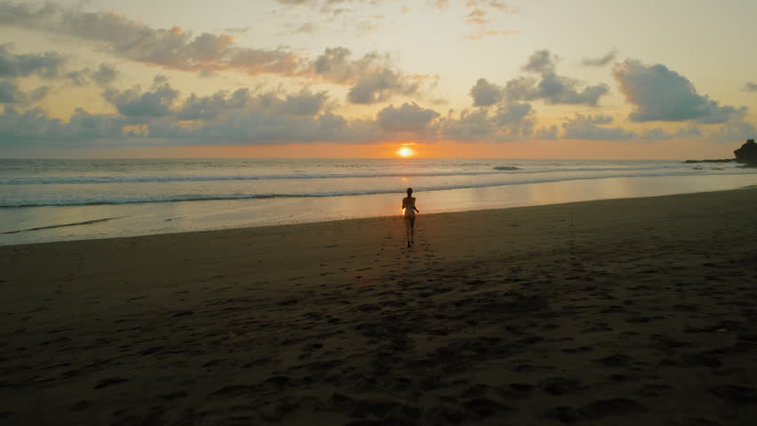 Silhouette of woman in swimsuit running on beach at sunset in Costa Rica
