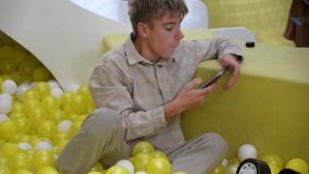 Teenager playing with ball pit and smartphone, lost in thought amidst sea of colorful spheres, reflecting on digital connection. - Powered by Shutterstock - Get 15% off with code: PIKWIZARD15