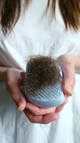 Close up of female hands cleaning a hairbrush full of fallen brown hair, demonstrating a problem with hair loss, thinning, hormonal changes, or alopecia in a conceptual health video. Vertical
