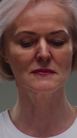Portrait: close up view of face of elderly woman with blue eyes and wrinkled skin texture. Senior retired female, grey hair. Upper face of old caucasian person. Headshot, shirt, natural aging features