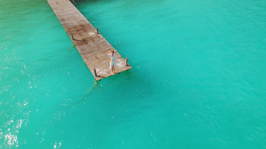 Woman standing on wooden pier over turquoise lagoon in Bacalar Mexico