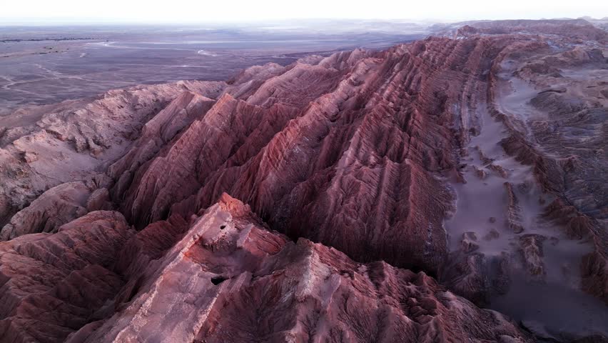 Aerial view over dramatic sharp ridges of eroded red rock formations in a vast arid desert plain at dusk. Valle de la Luna, San Pedro de Atacama, Chile
