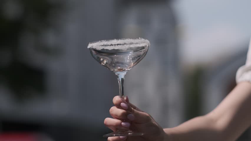 Hand holding a salted rim cocktail coupe as a clear liquid is poured into it outdoors