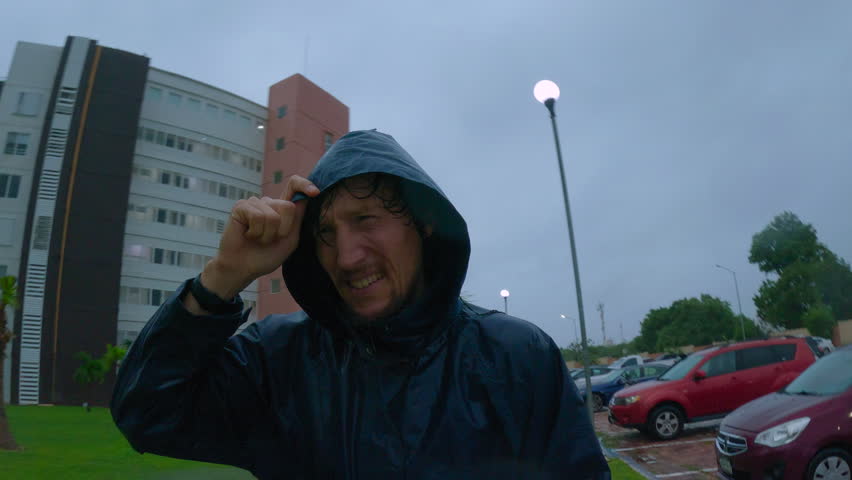 Middle aged man in a blue jacket walks through heavy rain and strong wind during a tropical storm. Dramatic real life moment showing resilience against extreme weather and effects of the climate
