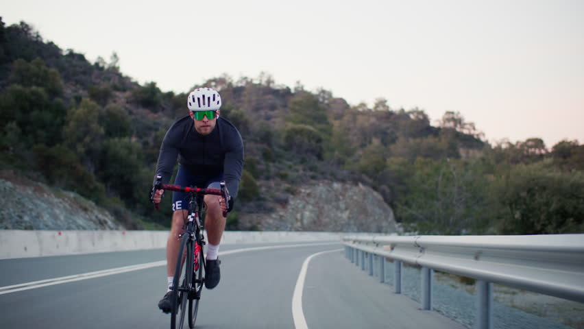 Athletic cyclist is cycling in the mountains landscape. Guy rides a bike on the highway, doing sports.