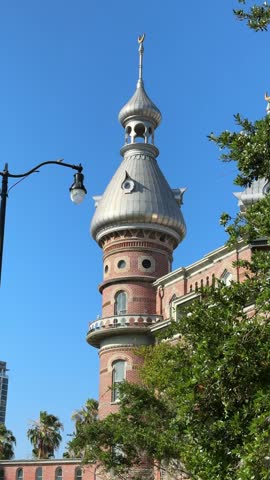 An ornate architectural tower stands tall above green trees under a clear blue sky. The scene highlights historic design and warm Florida daylight.
