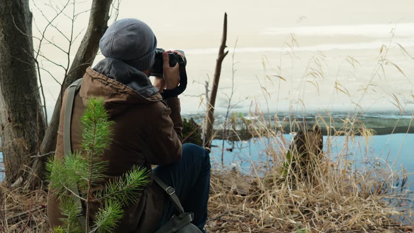 A male photographer captures the spring beauty on the shore of a forest lake, where the ice melts. Love of nature, creativity and inspiration.