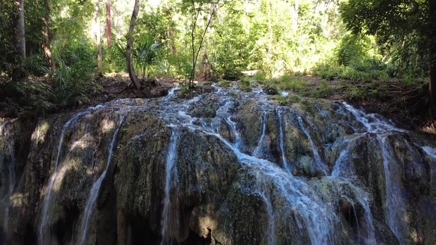 Thermal waterfall near Lake Izabal in Guatemala. Aerial close shot tilts downward following multiple hot water streams cascading into river, no people