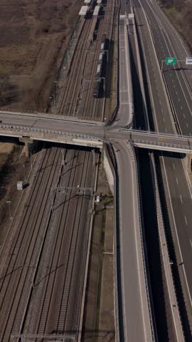 High-angle drone shot showing a modern passenger train traveling on railway tracks next to a multi-lane highway with an overpass interchange