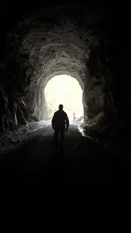 Man walking alone through a dark tunnel towards the light