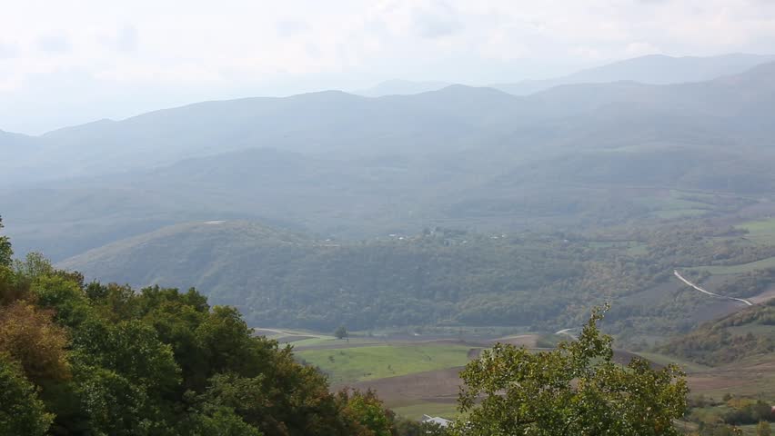 A breathtaking, hazy view of rolling hills and mountains in autumn. Terraced fields and scattered trees create a serene, expansive natural landscape.