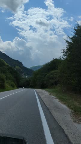 Driving along a scenic mountain road, surrounded by lush greenery and under a cloudy sky, showcasing the natural beauty of the landscape