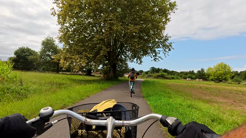 Pov footage of a person riding a bicycle and following another cyclist on a paved trail through the green countryside of azur, landes, france during a sunny summer day on vacation