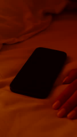 Hand Gently Touching Smartphone Alarm Screen Reading 6 AM While Lying on Bed in Soft Orange Light Morning Laziness.