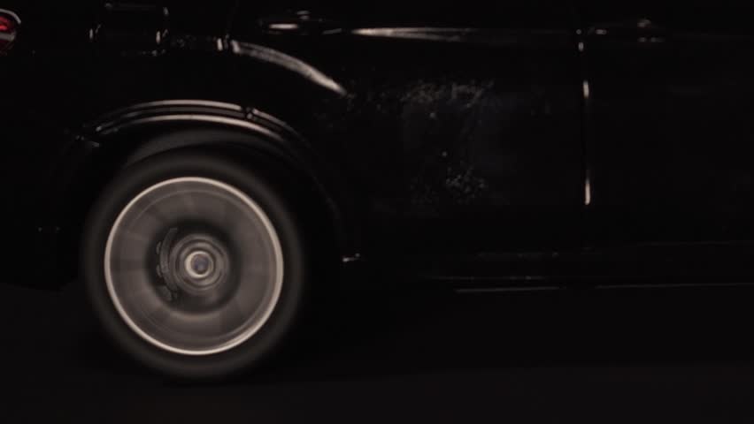 A closeup of a black toy luxury SUV running on a treadmill simulating a roadtrip at night