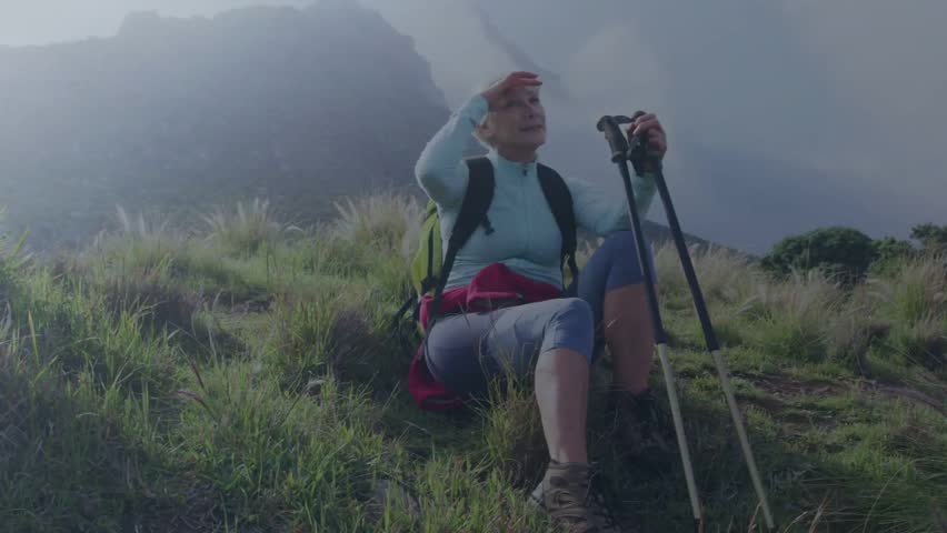 Woman hiker seeing ridge, shading eyes, bracing poles, cloud layer crossing torso, prepping to move. Hiking, mountainside, landscape, horizon, mist, grass, boots