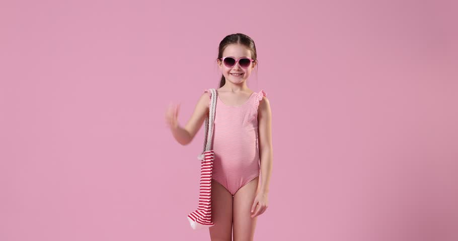 Little girl in swimsuit with beach bag on pink background