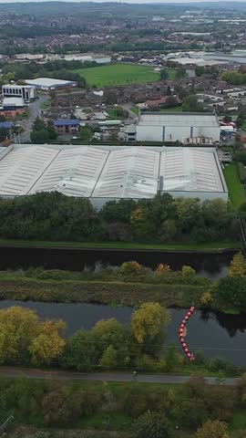 Vertical screen Highangle Shot Of Leeds Rooftops And Canal, Overcast Sky With Muted Light, Reflective Warehouse Roofs, River Edged By Trees In Autumn Colours, Red Buoy Chain Marking Water,