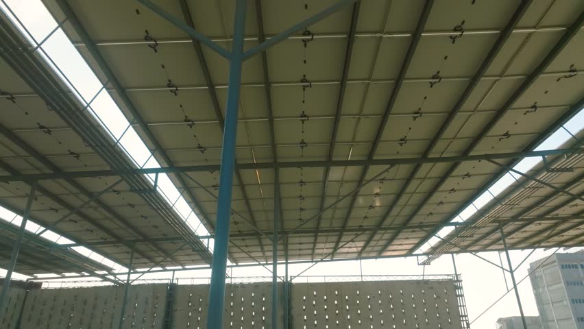 Upward tilted right tracking aerial inside a Karachi factory with the ceiling covered in solar panels during a sunny morning.