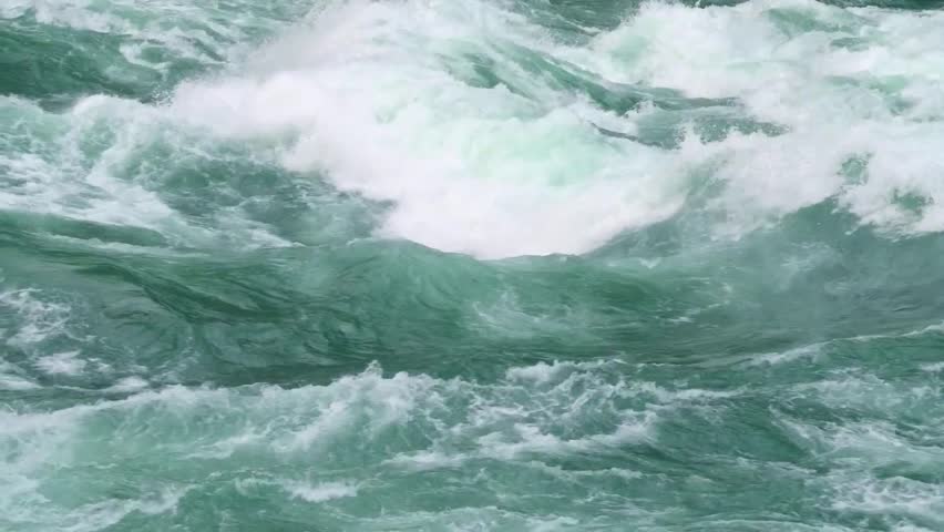 Powerful churning water rapids with white foam and spray in a fast flowing river landscape.