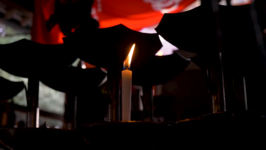Slow motion close-up of a candle flame burning a glowing light inside a small prayer spiritual shrine at Fushimi Inari Shrine hiking forest trails in Kyoto traditional city Japan history and tourism