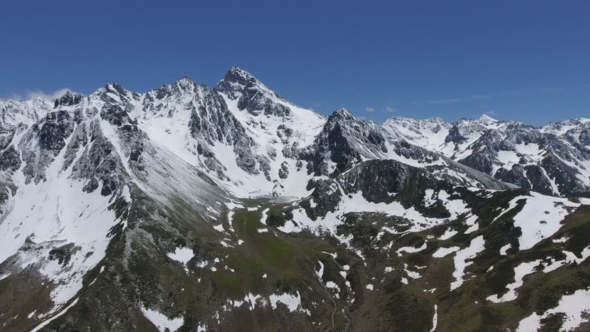 Aerial view of snowy Patagonia mountains with glacial tarn lake near Argentina Chile border. Alpine ridge panorama featuring ice covered peaks, cirque pond, rugged range on South American frontier. Patagonia, Mountains, and Glacier reveal landscape character, environmental detail, and a strong sense of place. The footage supports nature, travel, scenery, environment, and destination related searches. Clear natural textures and recognizable terrain make the clip useful for documentary and tourism projects.