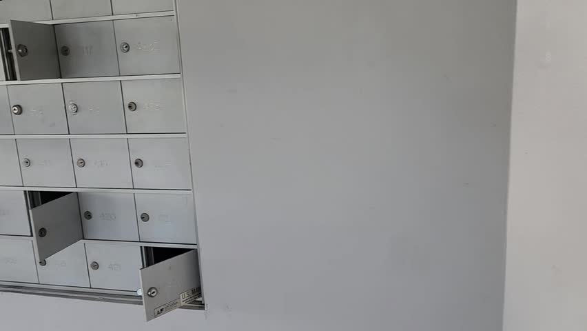 Multiple metal apartment mailboxes with several doors left open in a residential building hallway. Organized grid of numbered boxes with visible compartments.