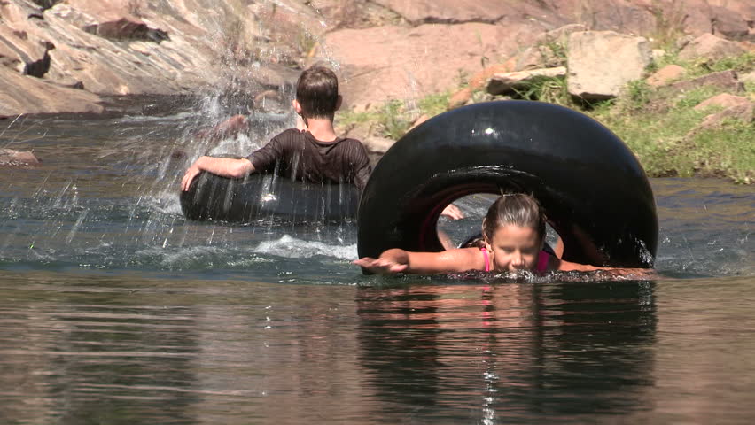 Girl spinning around on inflated tubes and having fun with boy in a river.