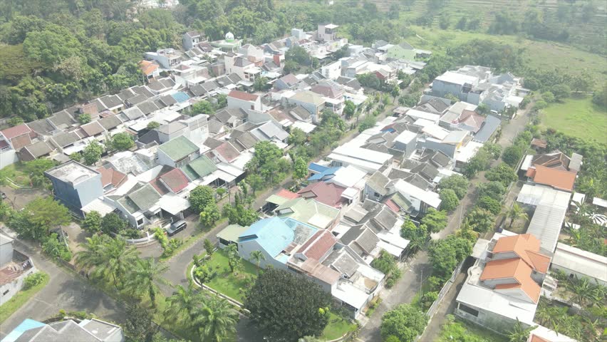 Aerial view of a dense suburban residential area with misty green hills in the background.