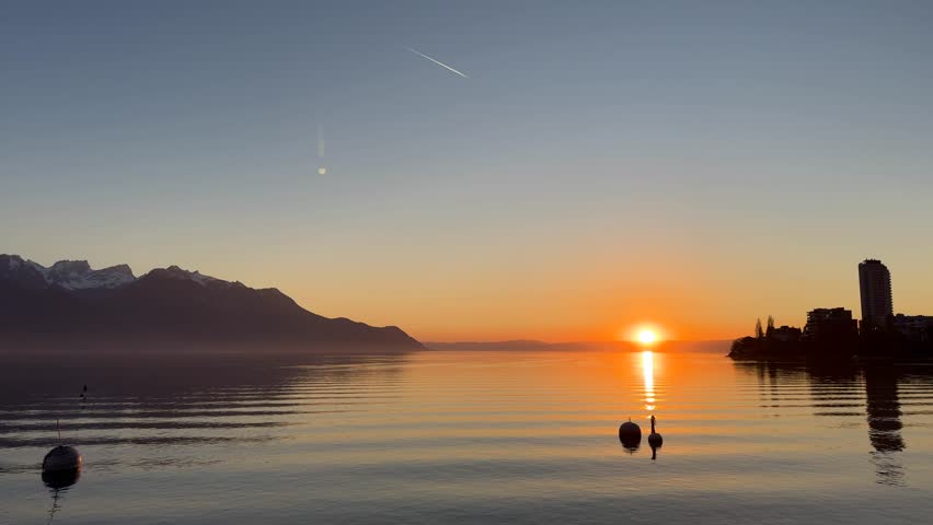 Peaceful sunset over Lake Geneva in Switzerland with Alps mountains in the background and calm water reflections, creating a serene and relaxing atmosphere.