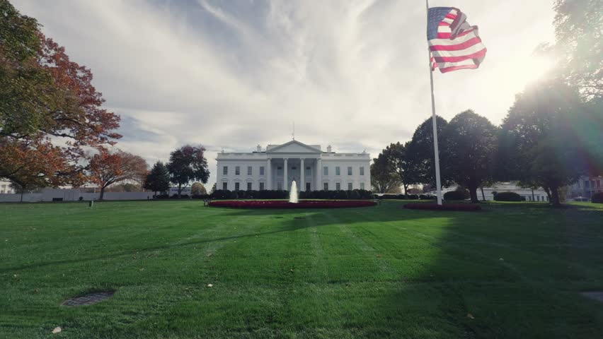 Cinematic footage of the White House in Washington, D.C., featuring the beautiful South Lawn fountain and the American flag waving proudly from the roof.