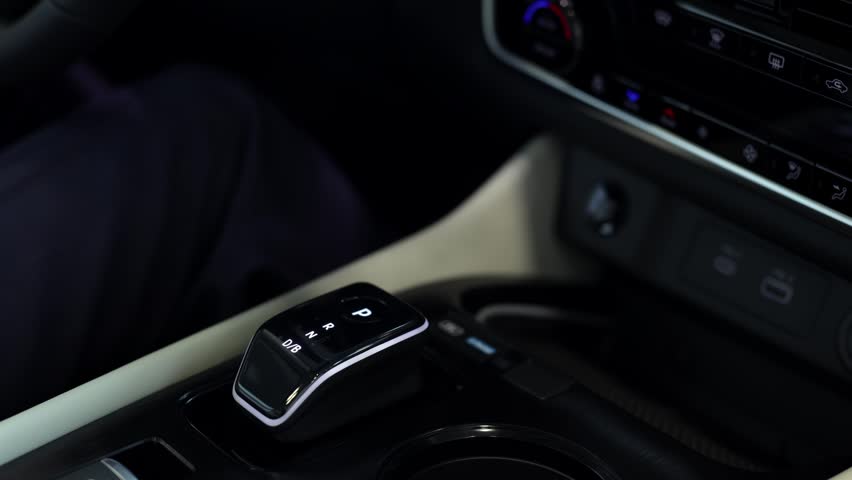 Man adjusting gear shift in modern car interior, showcasing automotive technology concept.
