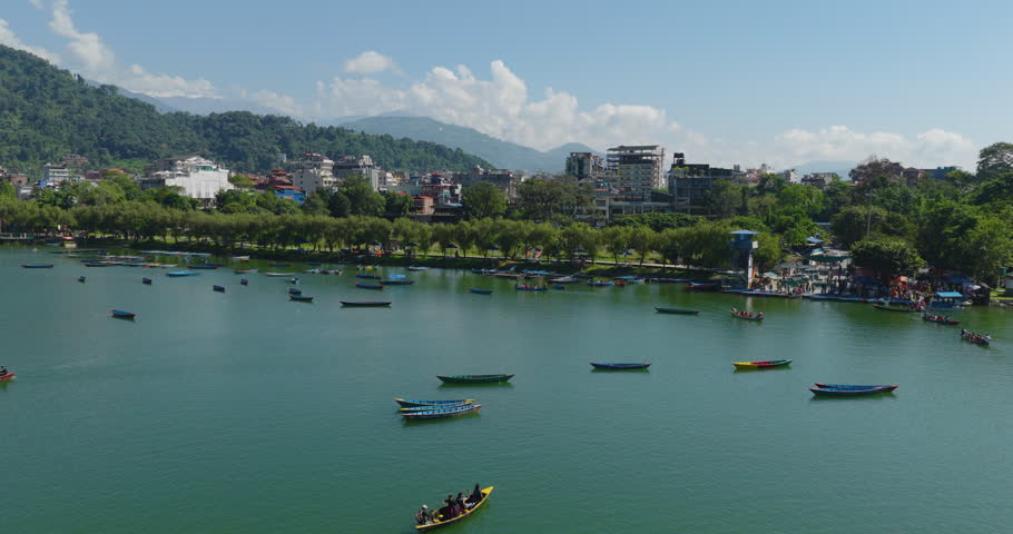 Aerial shot of colorful boats floating along the bank of calm blue Phewa Lake under a cloudy sky at Lakeside Pokhara Nepal.