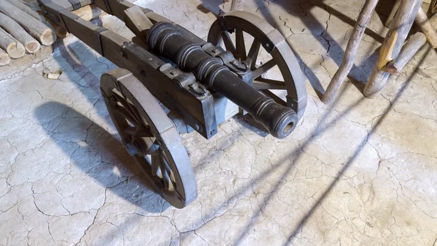 Cast iron Cossack cannon on a wheeled carriage on clay floor of a historical museum.