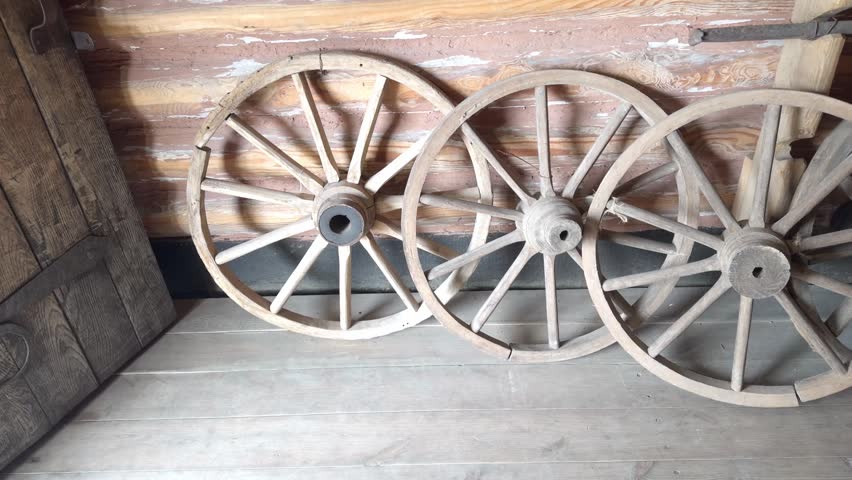Four antique wooden wagon wheels leaning against a log wall in a barn.